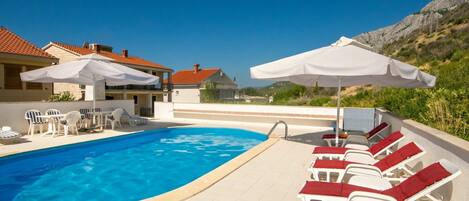 Zona de piscina amb gandules i ombrel·les, envoltada d'edificis amb teules vermelles.