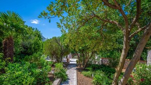 A stone pathway flanked by lush greenery and trees, leading to a building with a white facade. - Beautiful  villa for 12 people with WIFI, TV and terrace (Crikvenica)