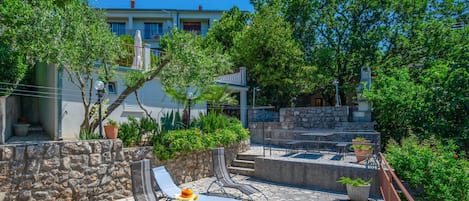 A courtyard with stone flooring, outdoor seating, and lush greenery.