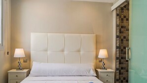 Une chambre d’hôtel avec un grand lit, deux tables de chevet avec des lampes et une douche en verre.