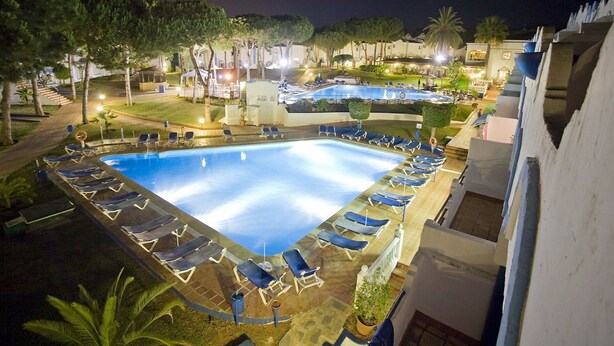 Une piscine dotée de chaises longues et offrant une vue sur les environs, de nuit.