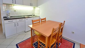 A compact kitchen with white cabinets, a wooden dining table, and a red rug.