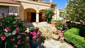 A Mediterranean-style villa with a stone courtyard, potted plants, and a clear blue sky.