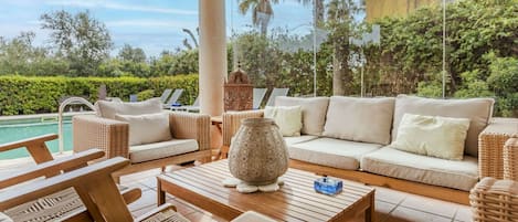 Uma área externa ensolarada com mobiliário de vime, piscina e um vaso decorativo.