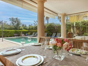 An outdoor dining area with a pool view, tables set with plates and glasses, and a vase with flowers.