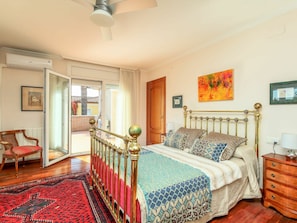 A bedroom with a bed, a wooden chair, a red and black patterned rug, a wooden dresser, and a ceiling fan.