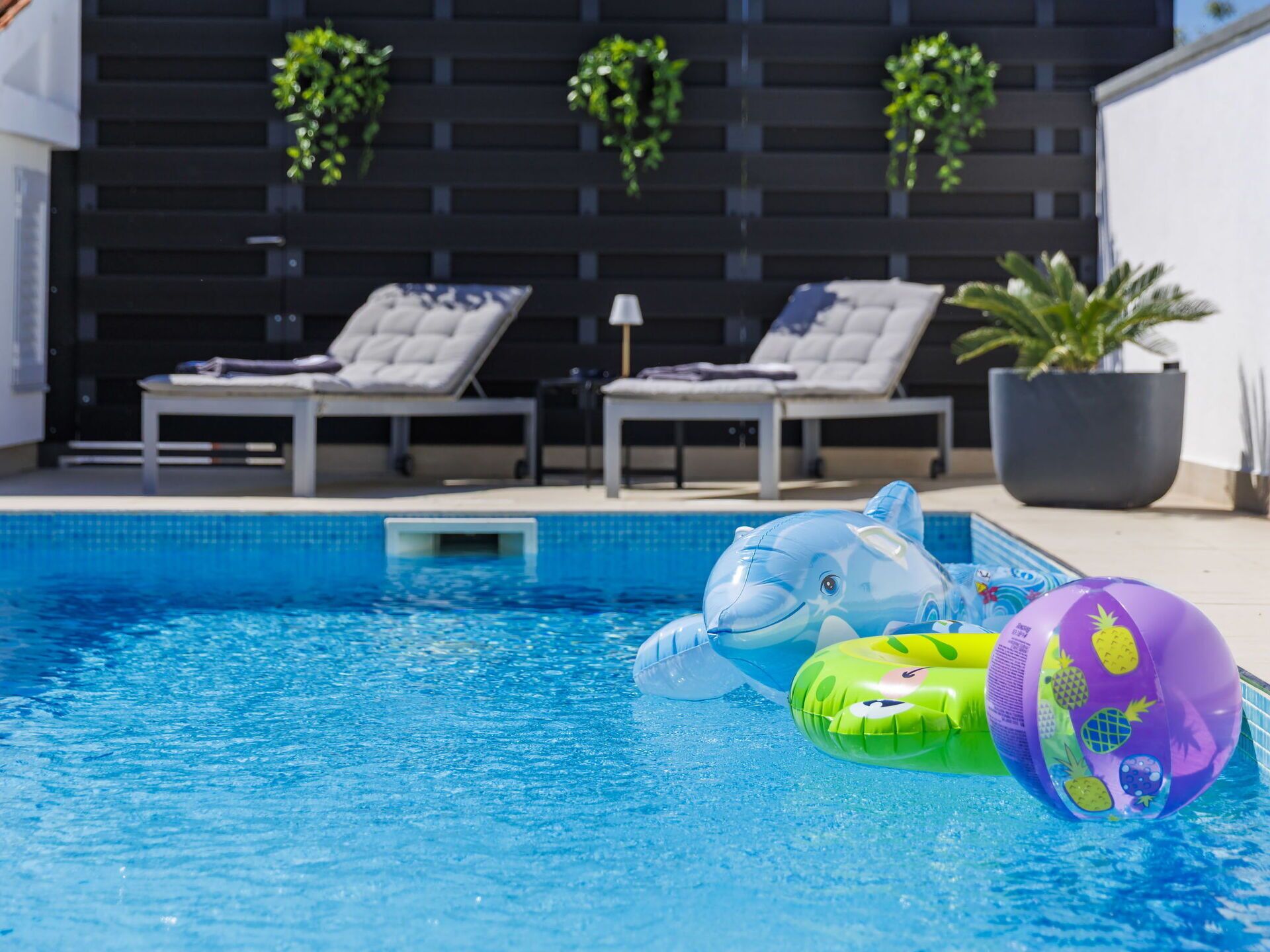 A swimming pool with lounge chairs and inflatable toys.