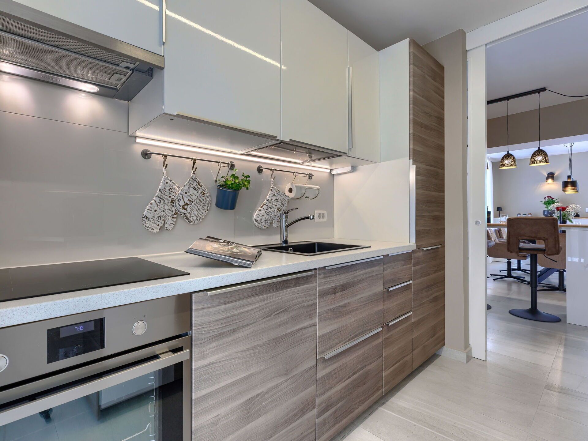 Una cocina moderna con extractor de acero inoxidable, horno empotrado, pileta y armarios de madera.