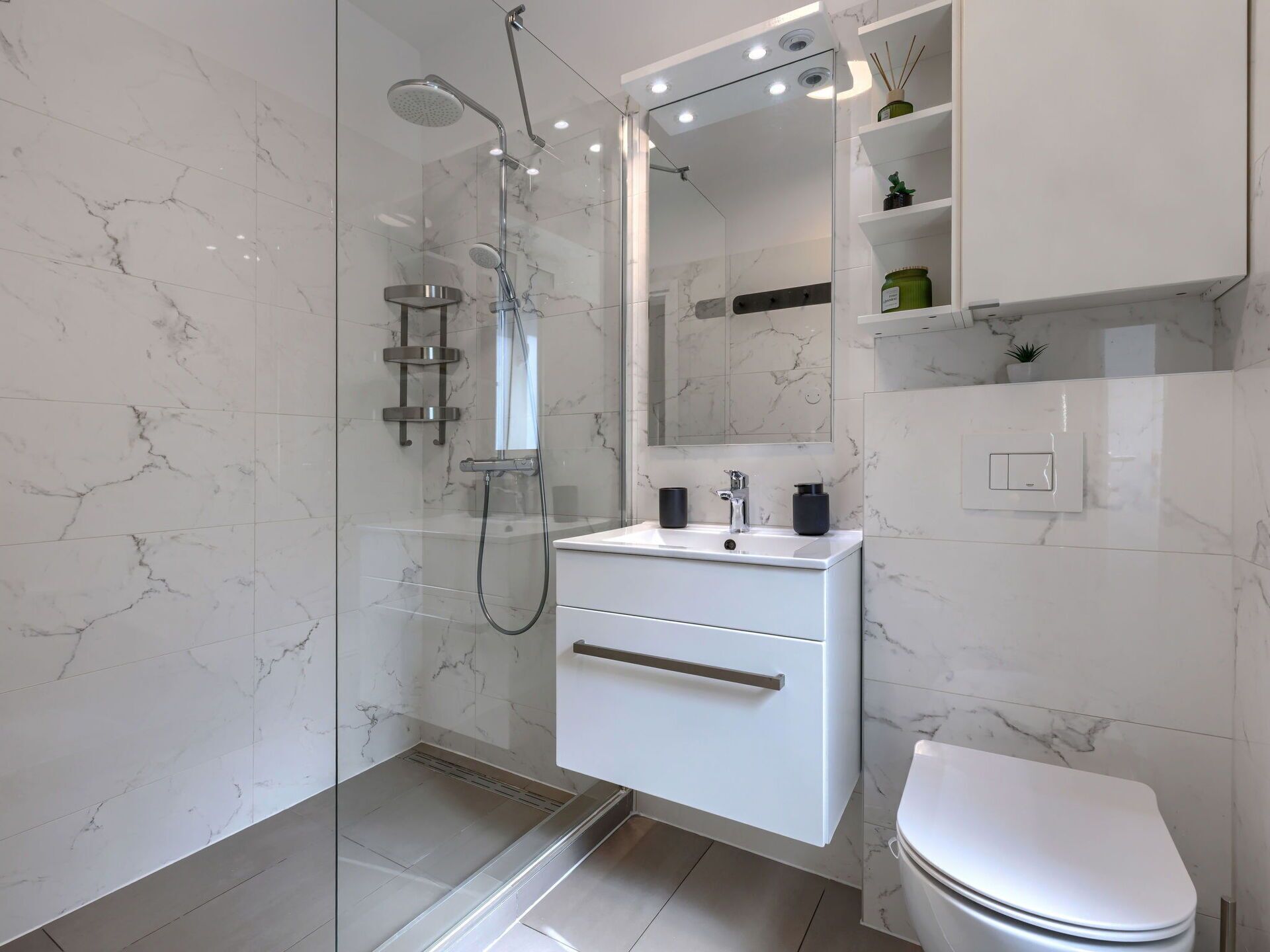 A modern bathroom with a glass-enclosed shower, a white sink with a mirror above it, and a toilet.