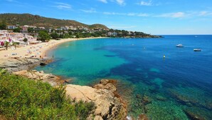 A coastal town with a sandy beach, clear blue waters, and buildings along the shore.