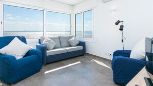 A modern living room with large windows, a sofa, a TV, and a lamp.