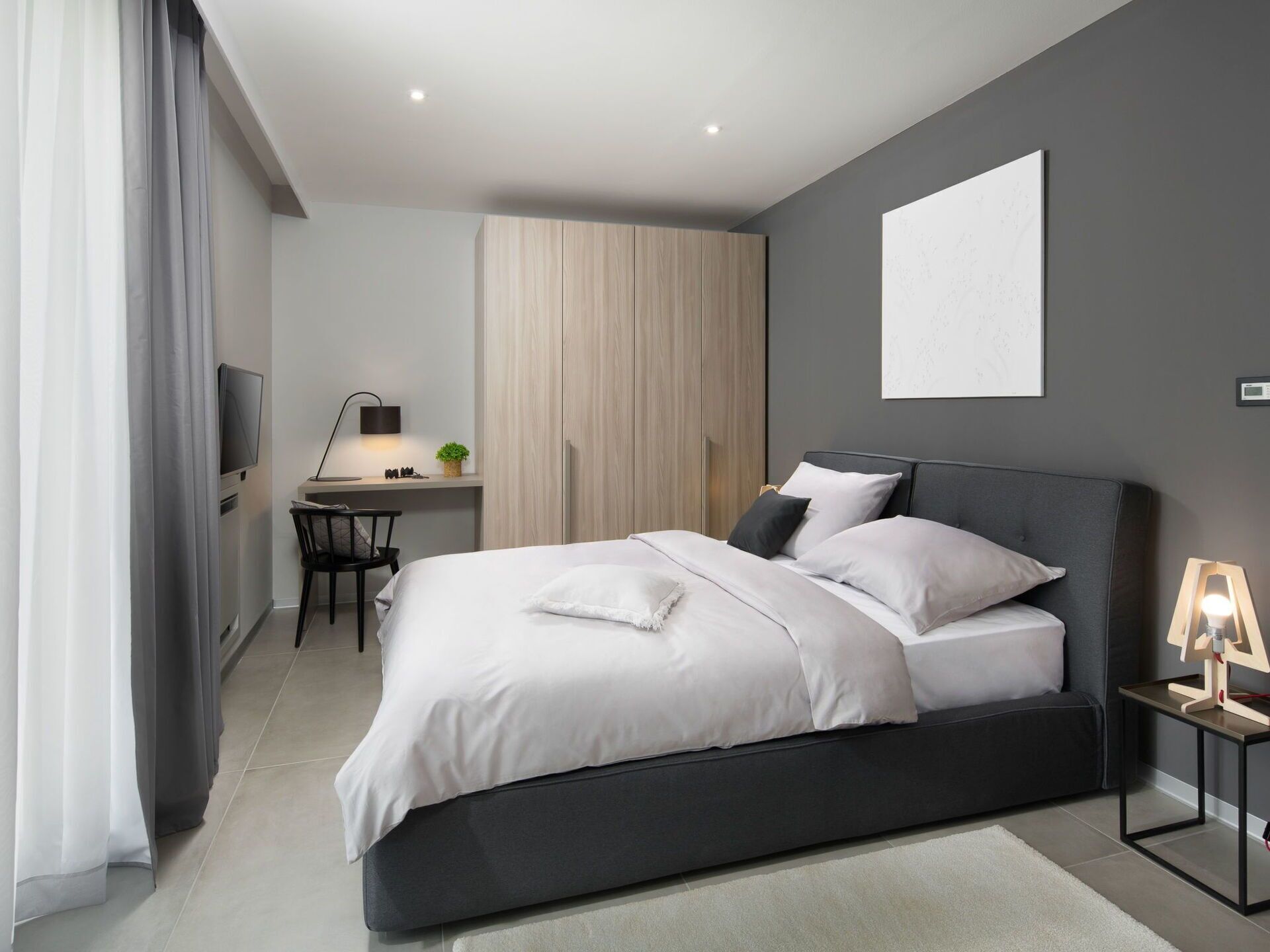 A modern bedroom with a large bed, a desk, and a wardrobe.