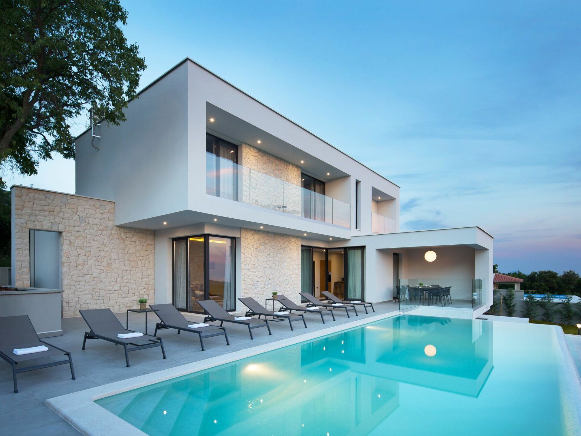 A modern two-story house with a swimming pool, outdoor seating, and a stone facade.