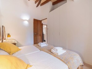 Un dormitorio con cama, mesita de noche, espejo, armario y puerta que da a otra habitación.
