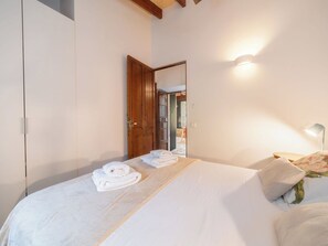 A bedroom with a bed, a wooden wardrobe, a mirror, and a bedside lamp.