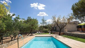 Ein rechteckiger Pool mit Holzterrasse, umgeben von Bäumen und einer Steinmauer.
