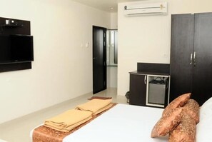 Een hotelkamer met een bed, een flatscreen televisie aan de muur, een kledingkast en een klein bureau met een stoel.