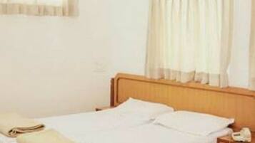 A single bed with a wooden headboard, a nightstand with a lamp, and a window with sheer curtains.