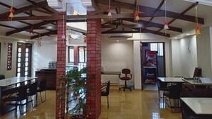 Une salle à manger spacieuse avec de hauts plafonds, des poutres apparentes et des décorations suspendues. On y trouve plusieurs tables et chaises disposées pour les repas.