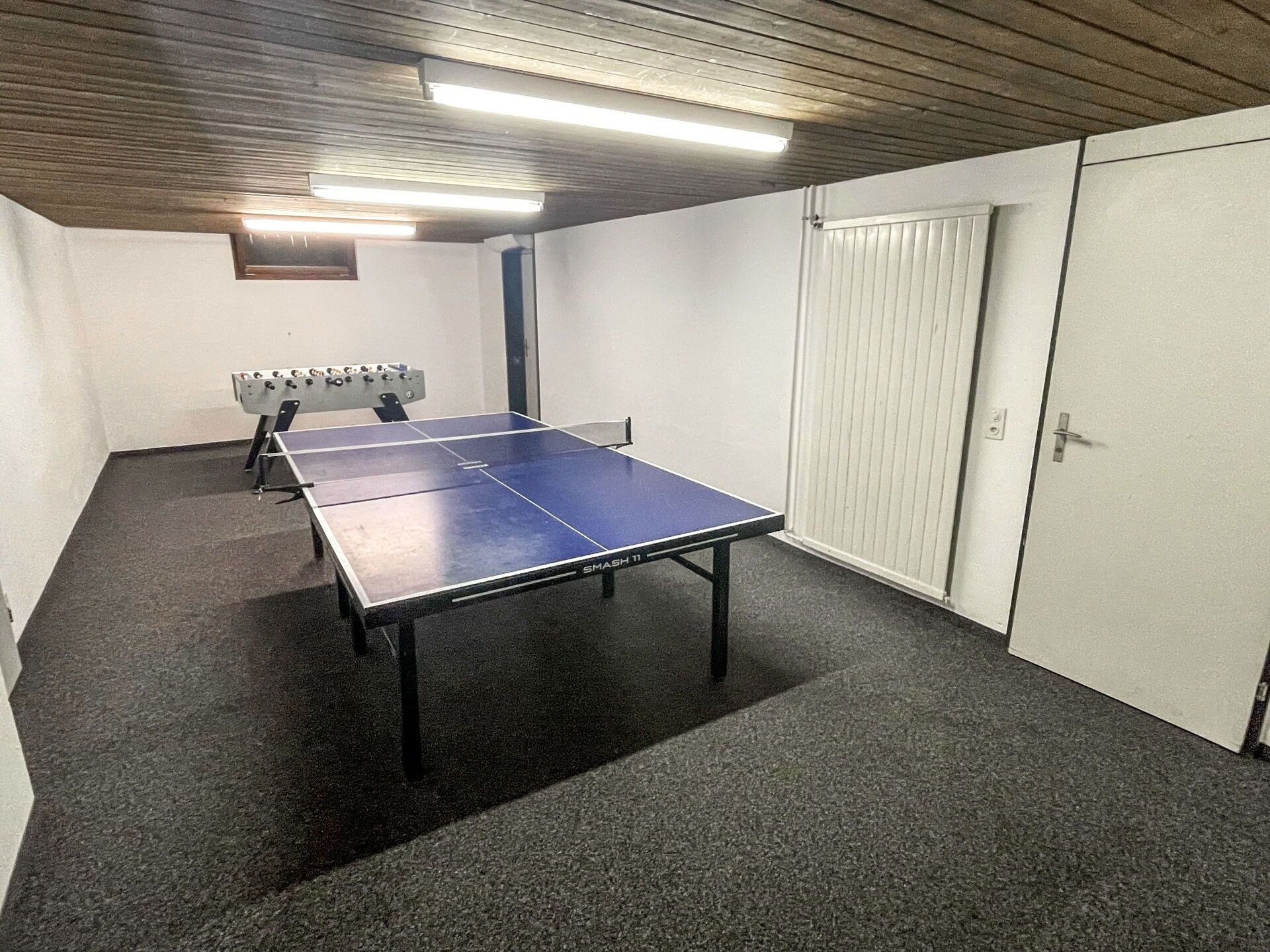 Una habitación con mesa de ping pong, mesa de futbolín y una puerta.