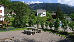 Un village rural avec une église blanche, une aire de jeux et un espace pique-nique, le tout entouré de verdure et de montagnes.