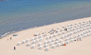 A beach with rows of white beach chairs and umbrellas, some occupied by people.