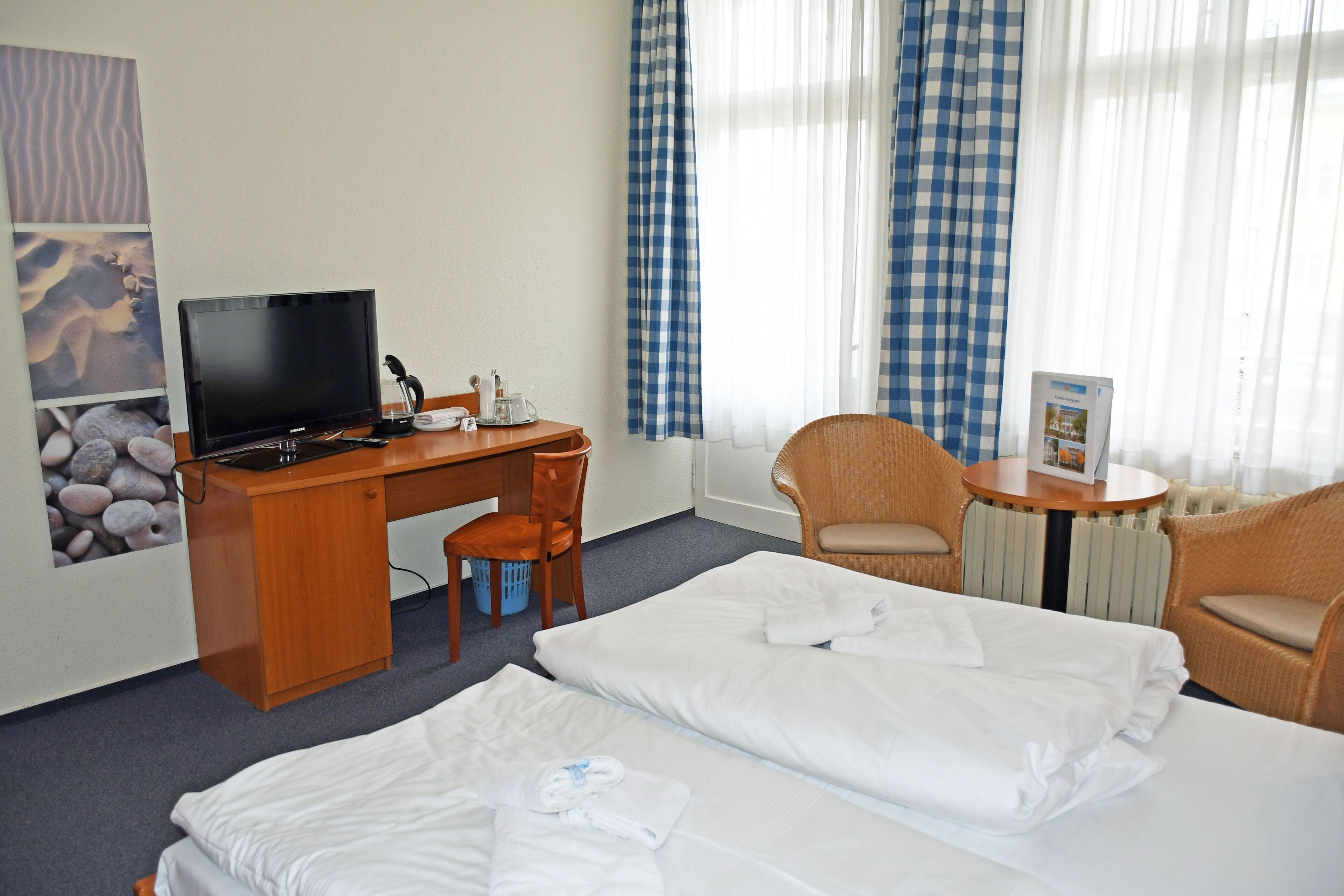 Ett hotellrum med två sängar, ett skrivbord med en dator, en stol och ett litet bord med en tidning.