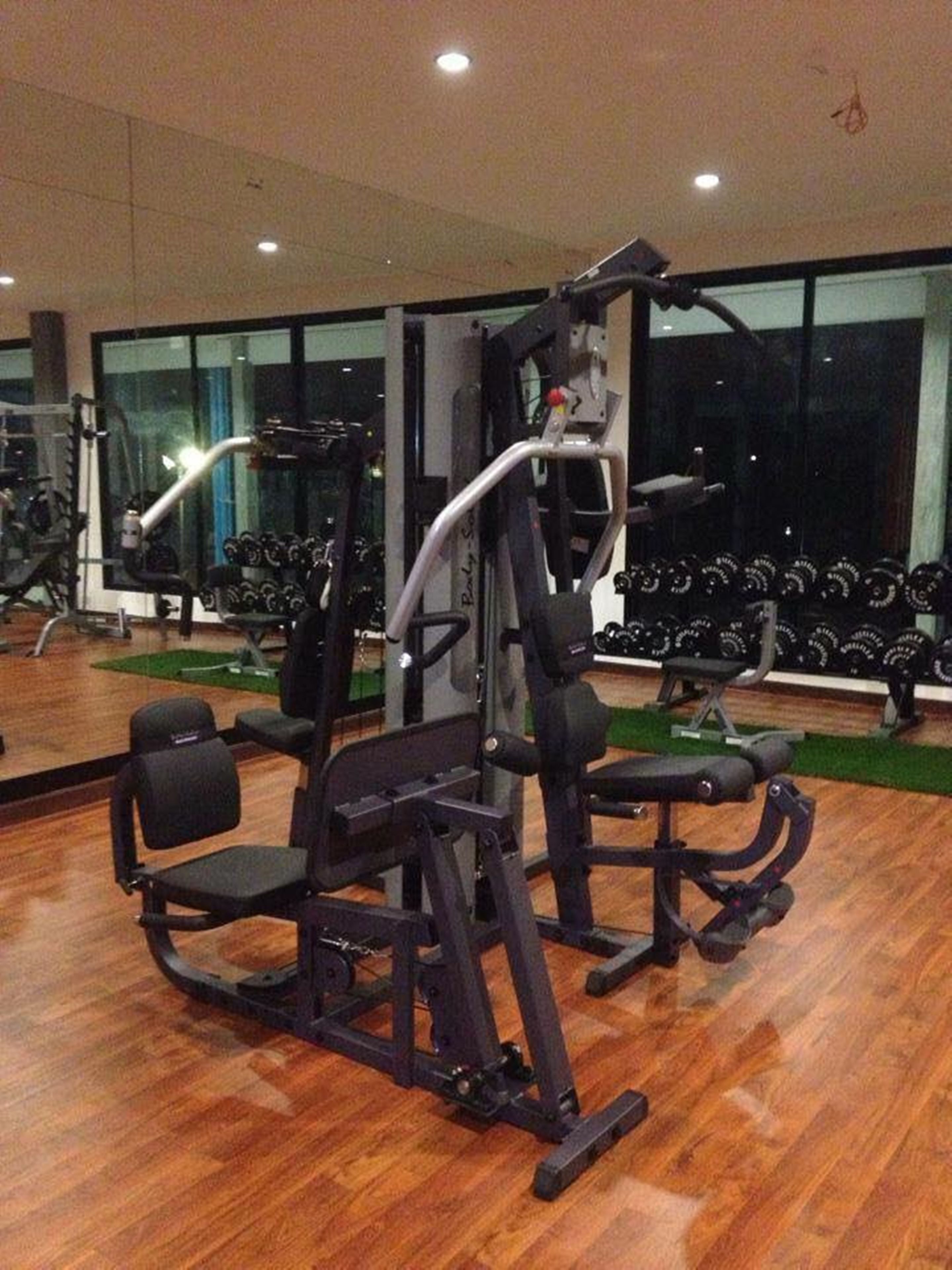 Academia com equipamentos de exercícios, um espelho e um suporte com halteres.