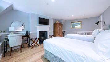 A bedroom with a bed, a desk, a chair, a fireplace, and a television.