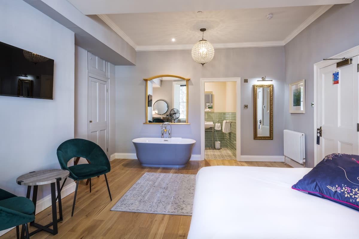 A modern bedroom with a large bed, a freestanding bathtub, a vanity with a mirror, and a chandelier.