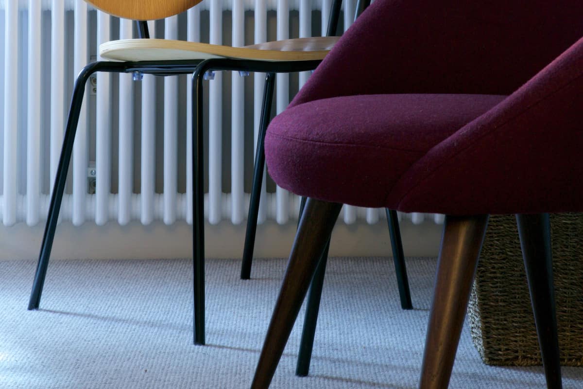 A room with a wooden chair, a purple armchair, a radiator, and a floor lamp.