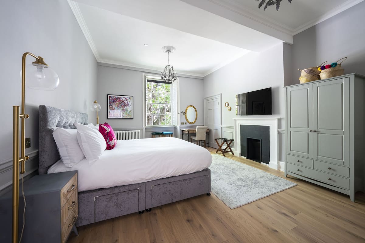 A bedroom with a large bed, a desk, a fireplace, and a wardrobe.