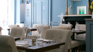 Un comedor con una mesa dispuesta para cuatro personas, rodeada de sillas tapizadas. Un espejo grande cuelga en la pared sobre la mesa, reflejando la habitación.