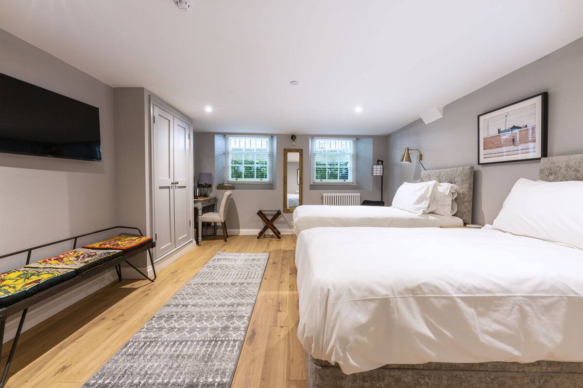 A bedroom with two beds, a desk, and a bench.