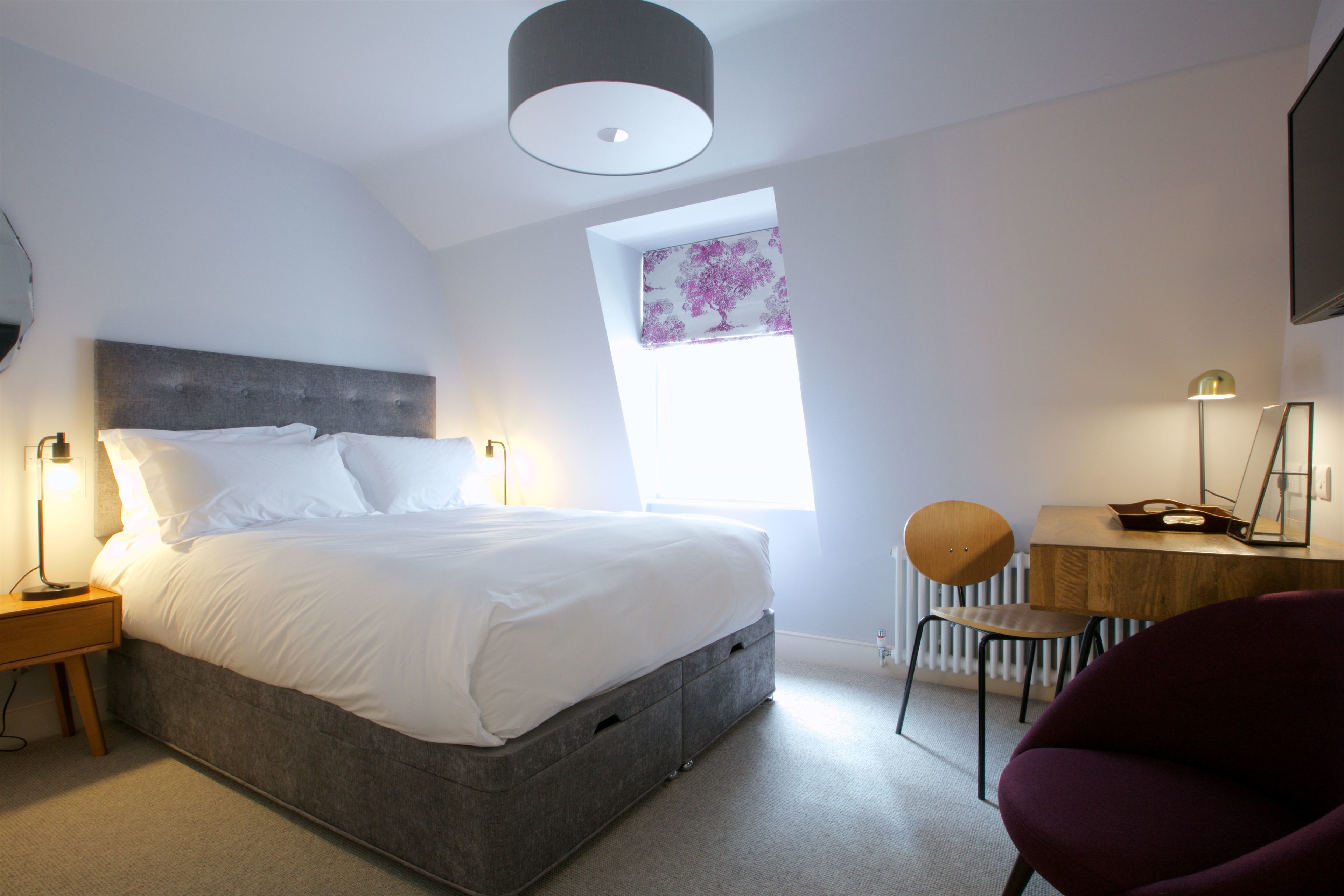 A modern bedroom with a large bed, a desk, a chair, and a window with a view.