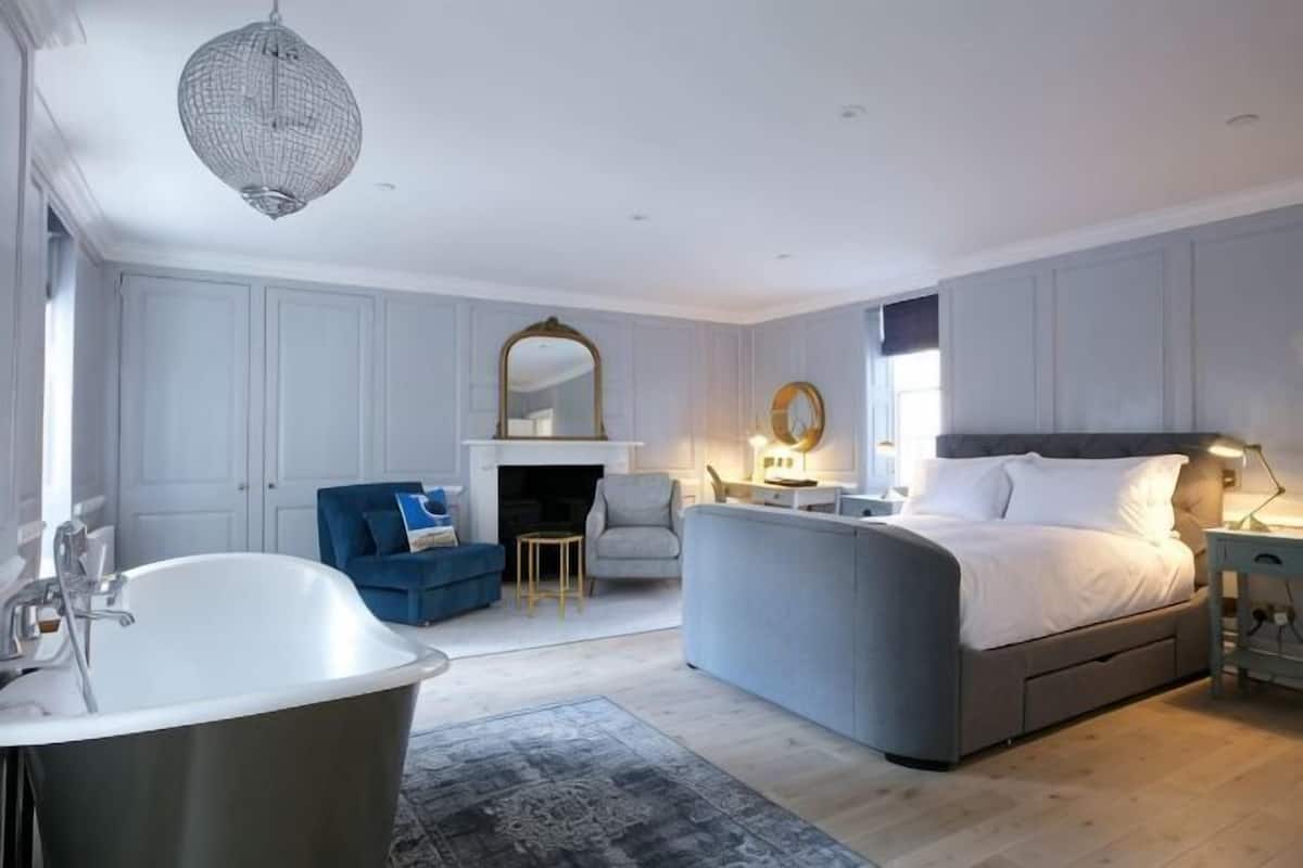 A bedroom with a large bed, a sitting area with a fireplace, a bathtub, and a dining table.