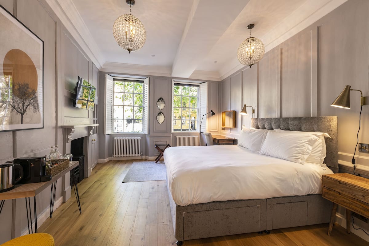 A bedroom with a large bed, a desk with a chair, a small table, and two pendant lights.