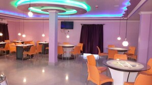 A restaurant with round tables and orange chairs, featuring a modern ceiling design with circular light fixtures. - Hotel Gitanjali Raiganj (Raiganj)