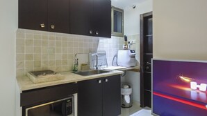 A compact kitchen with dark cabinets, a microwave, a coffee machine, and a sink.