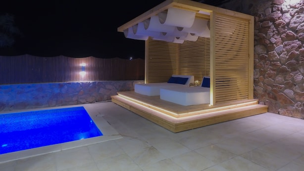 A modern outdoor pool area with a stone wall and wooden deck.