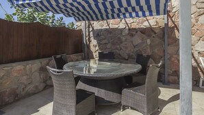 An outdoor patio with a round glass table and wicker chairs, a stone wall, and a wooden fence.