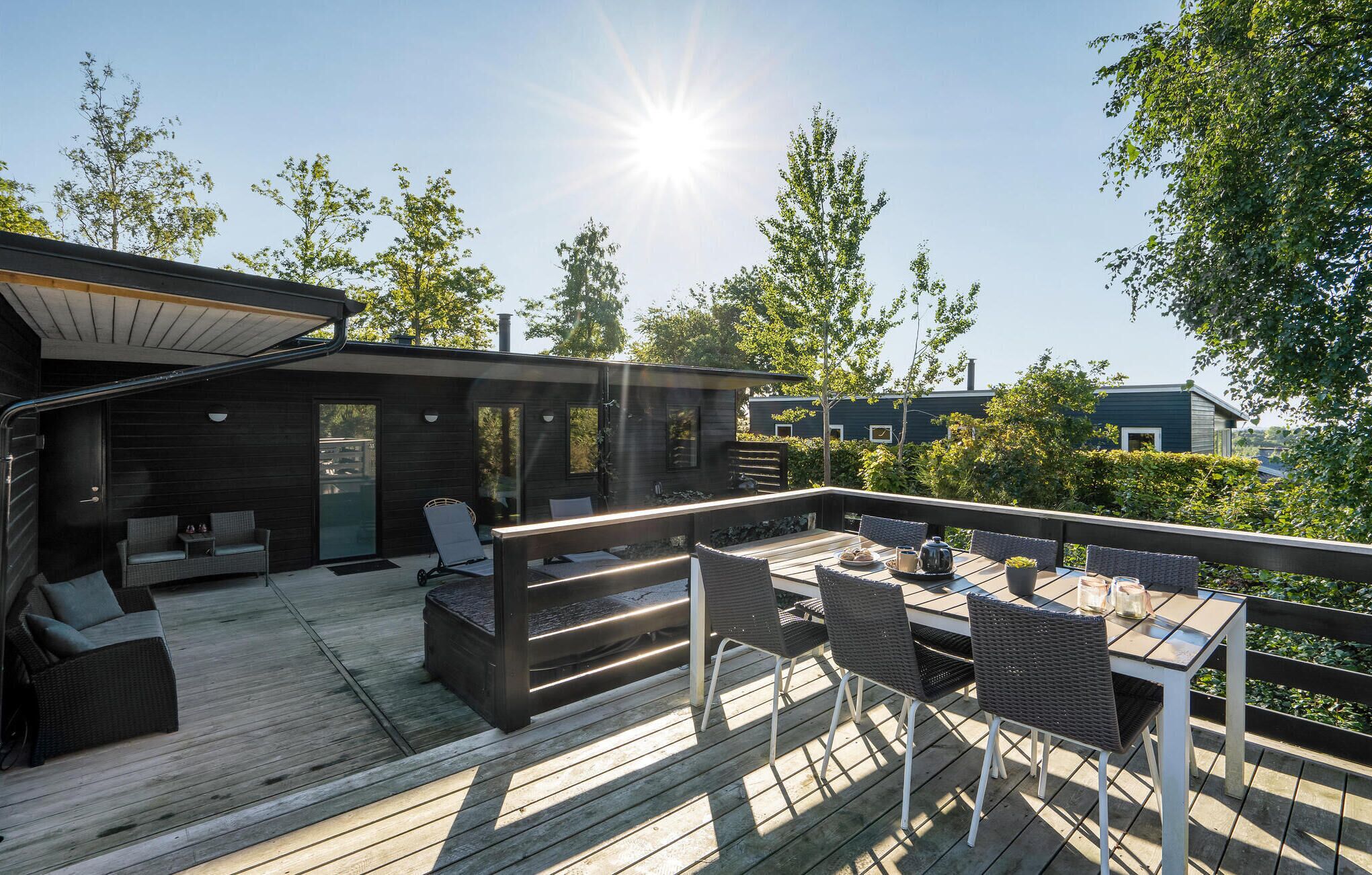 Eine Terrasse mit Gartenmöbeln, darunter eine Sitzecke und Stühle, mit Blick auf ein Wohngebiet mit Bäumen und blauem Himmel.