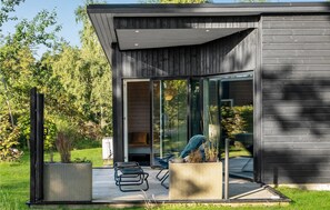 Et moderne hus med en glasdør, der fører ud til en terrasse med to stole og et lille bord.
