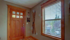 Eine Holztür mit Glasfenster, ein Fenster mit Jalousien und ein Paar Ski, die an der Wand lehnen.