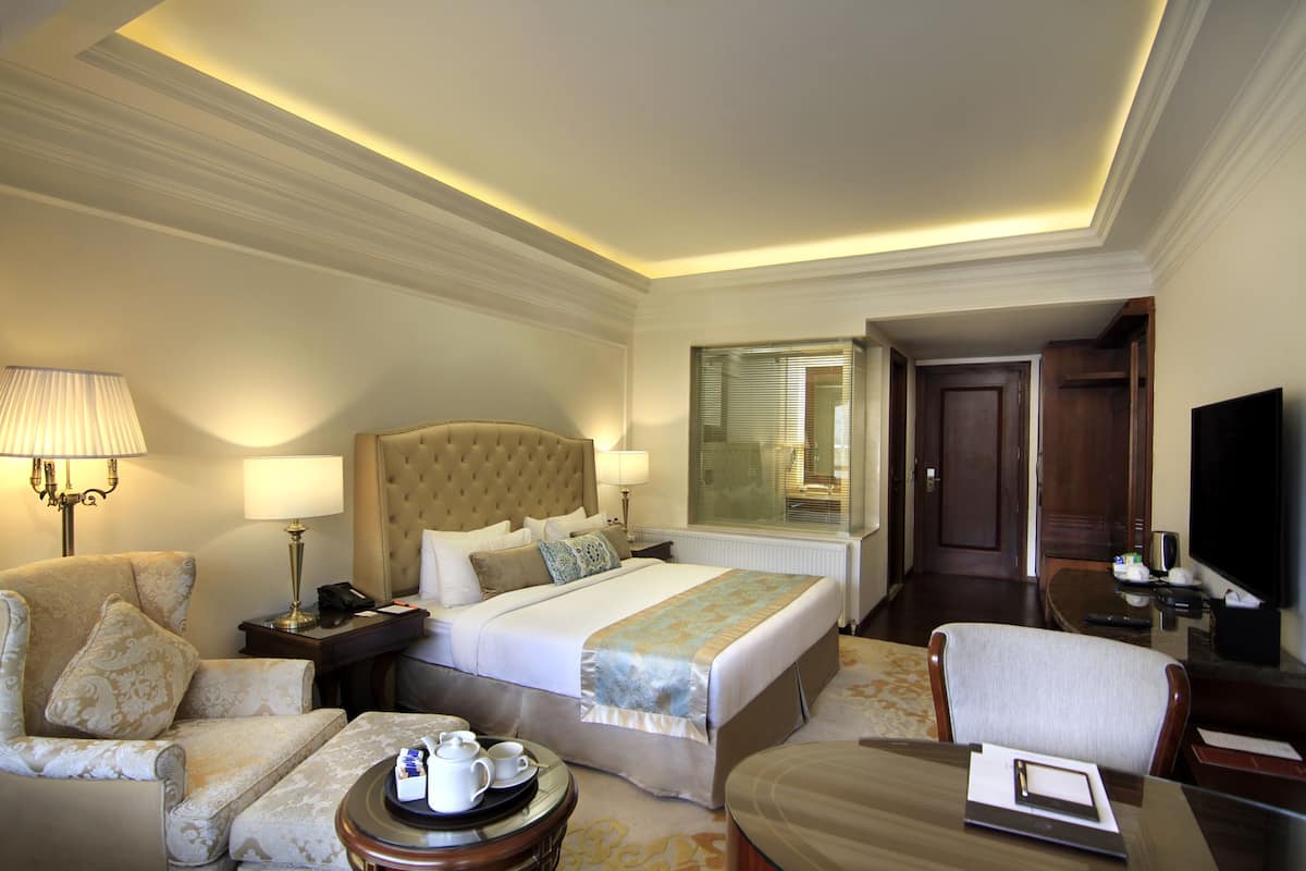 A hotel room with a large bed, a sitting area with a chair, a small table with a tray of items, and a television.