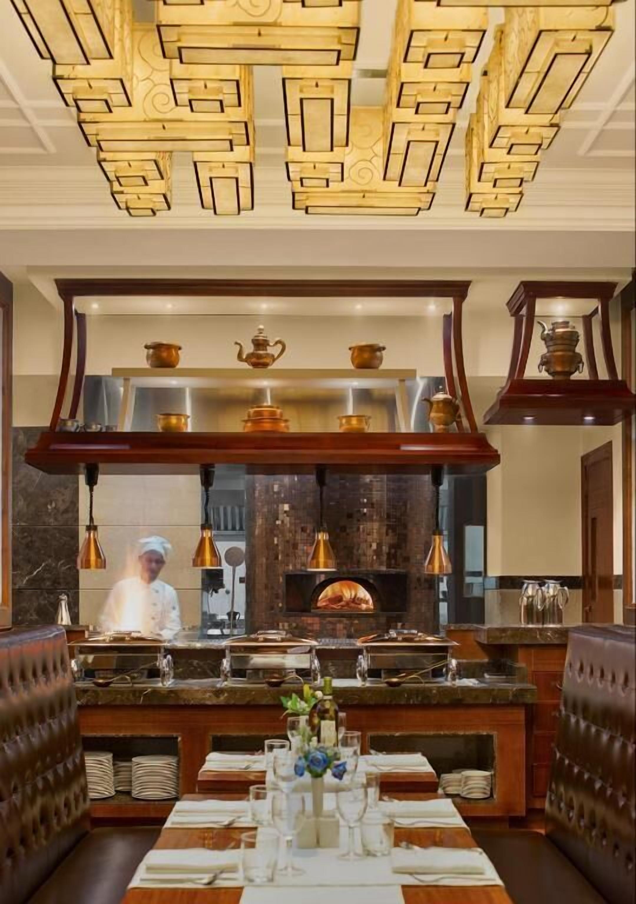 Un restaurante con un cocinero en la barra, un horno de ladrillo y una mesa de buffet.