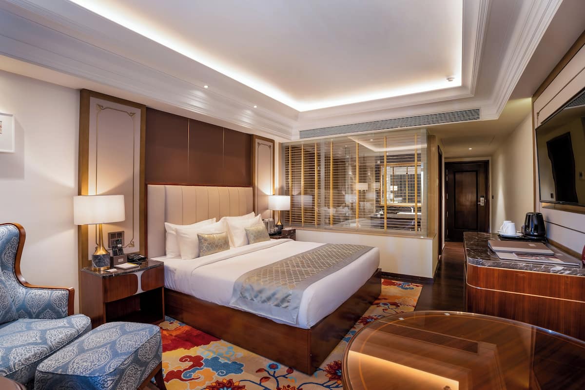 A hotel room with a large bed, a desk, a chair, and a TV.