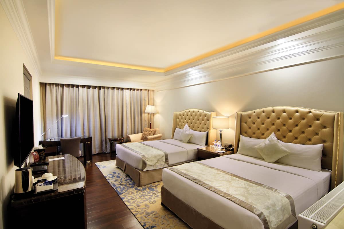 A hotel room with two beds, a TV, a desk, and a bathroom.