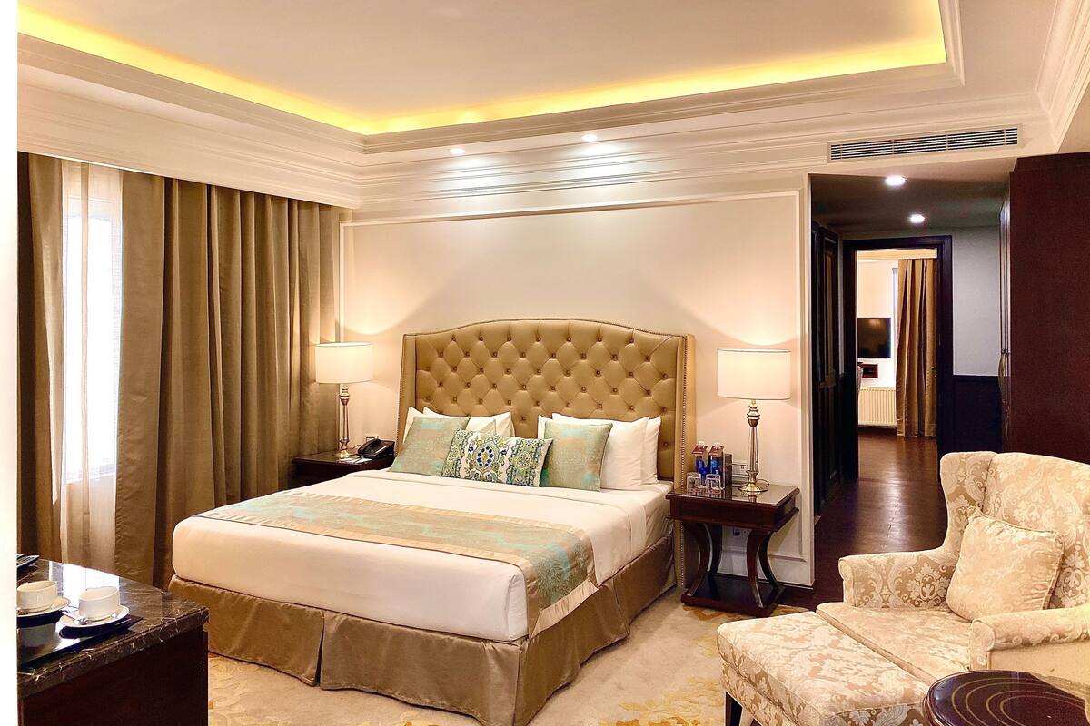 A hotel room with a large bed, two bedside tables, a chair, and a lamp.