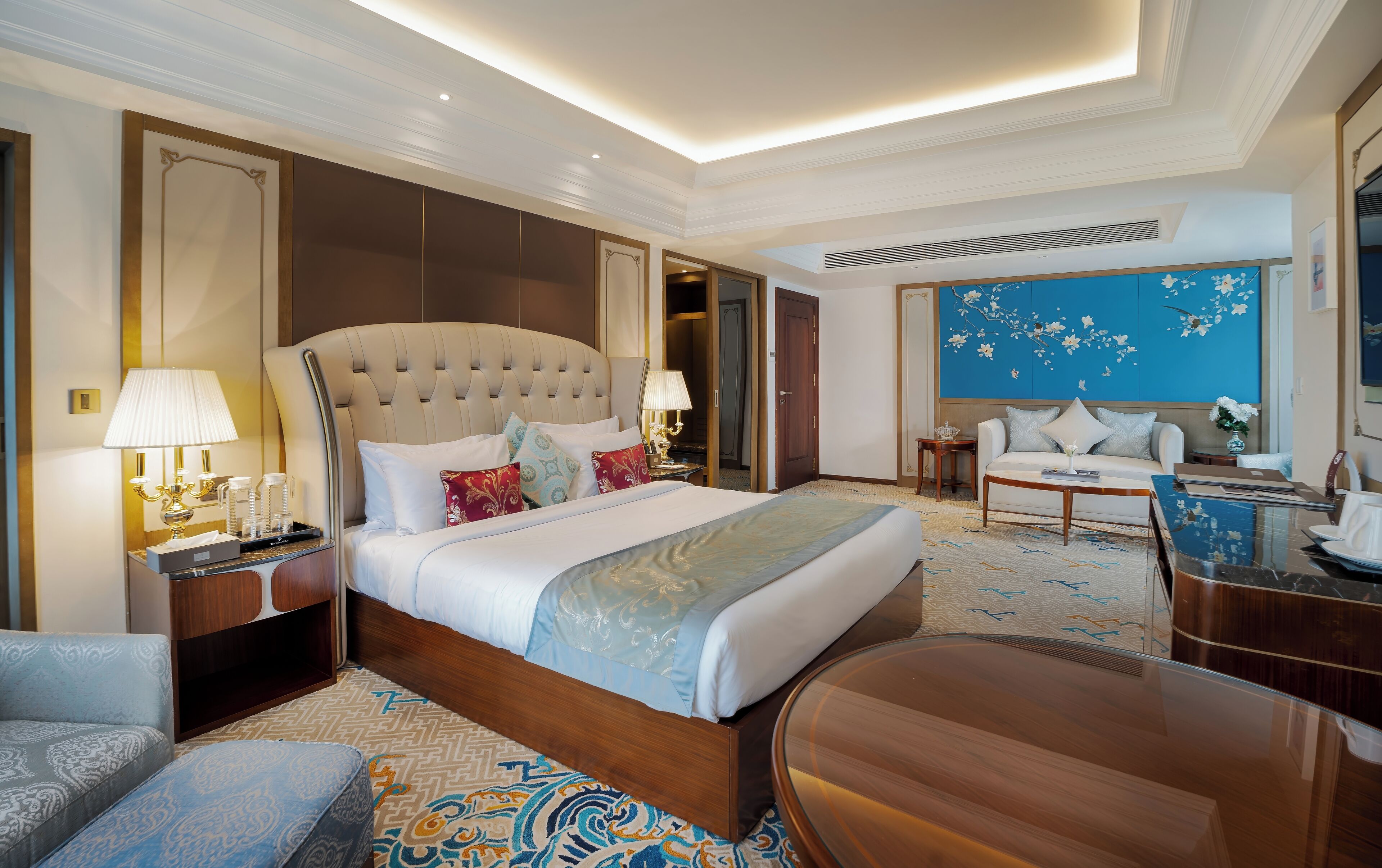 Une chambre d’hôtel spacieuse avec un grand lit, un coin salon comprenant un canapé et des fauteuils, une table à manger et un mur décoratif.